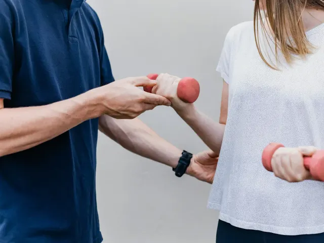 A physiotherapist guiding a woman through an arm exercise with light dumbbells