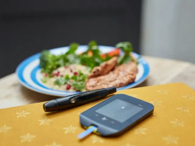 A plate of salad and grilled food beside a blood glucose meter