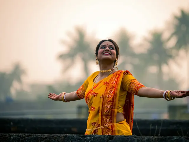 A smiling woman in a yellow saree with her arms open
